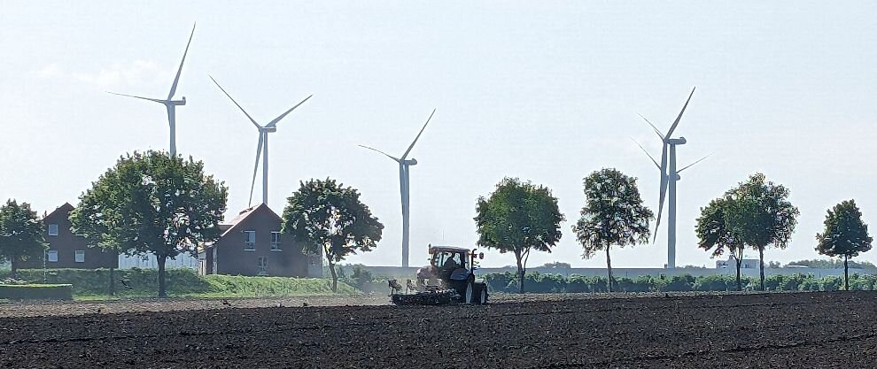 Foto eines Schleppers bei der Feldarbeit. Im Hintergrund Windräder Foto eines Schleppers bei der Feldarbeit. Im Hintergrund Windräder